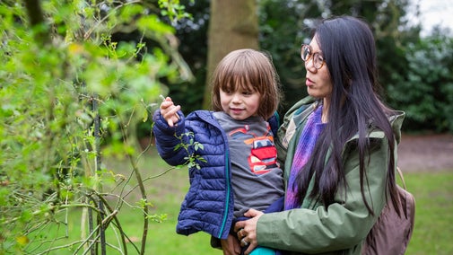 Woman holds a small child looking at leaf.